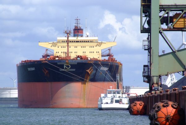 The image shows a large cargo ship docked at a Rotterdam port with the name "DOCEBAY" on the front two sides.